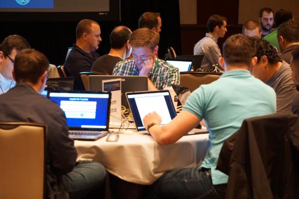 A lot of nerds sitting around a table and working on laptops. The room looks full of energy and makes you want to register for the next event.