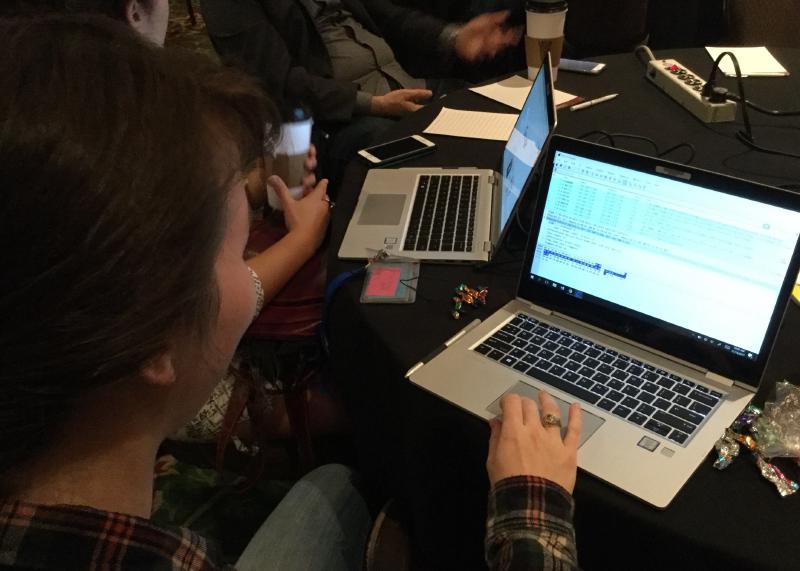 A photo looking over the shoulder of a woman using a laptop. The laptop is running WireShark, a popular network analysis tool. Other people are seated to her left, also using laptops.